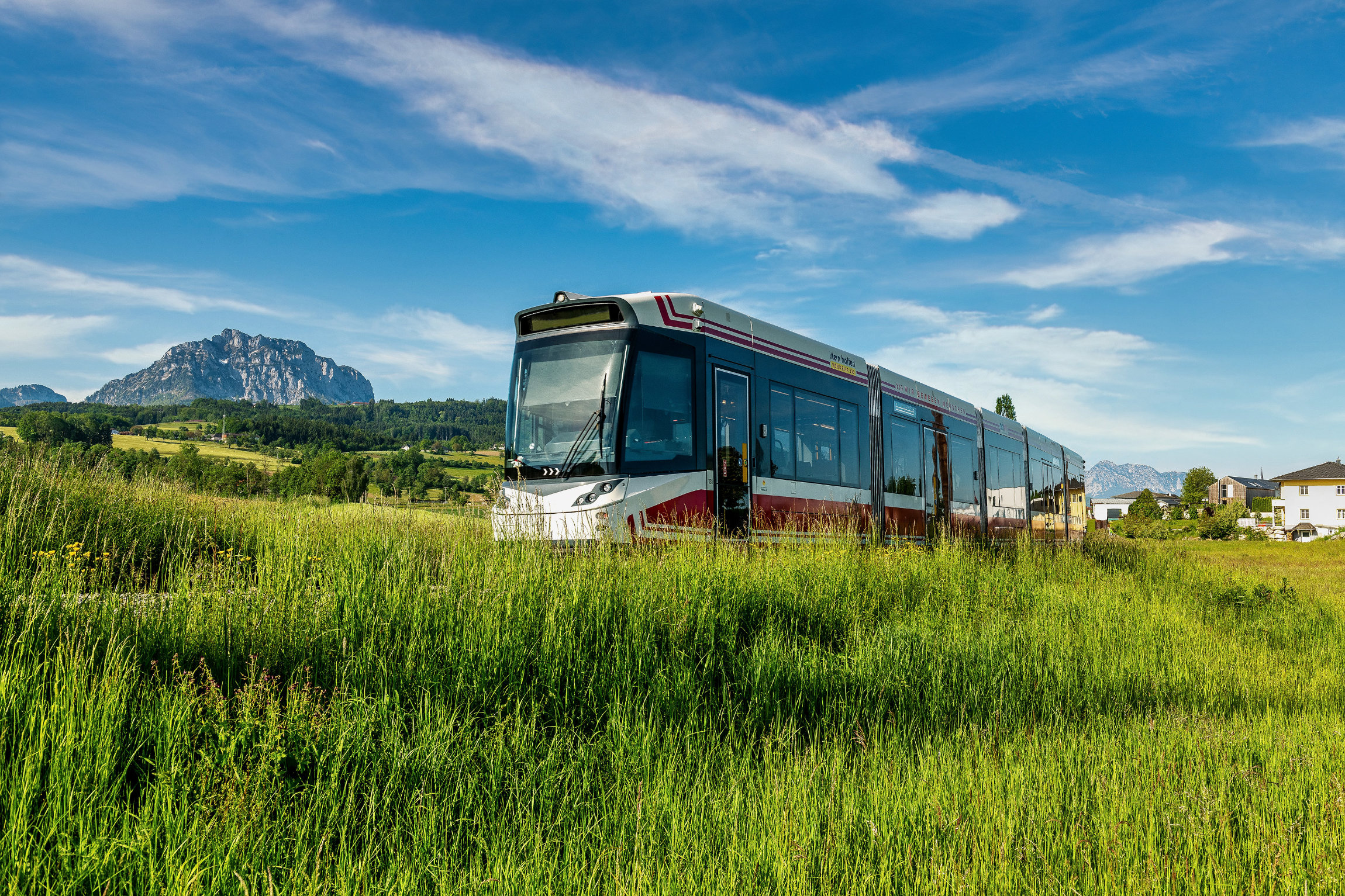 die Traunseetram in Gschwandt, im Vordergrund eine lange Wiese, im Hintergrund der Flachberg und der Traunstein