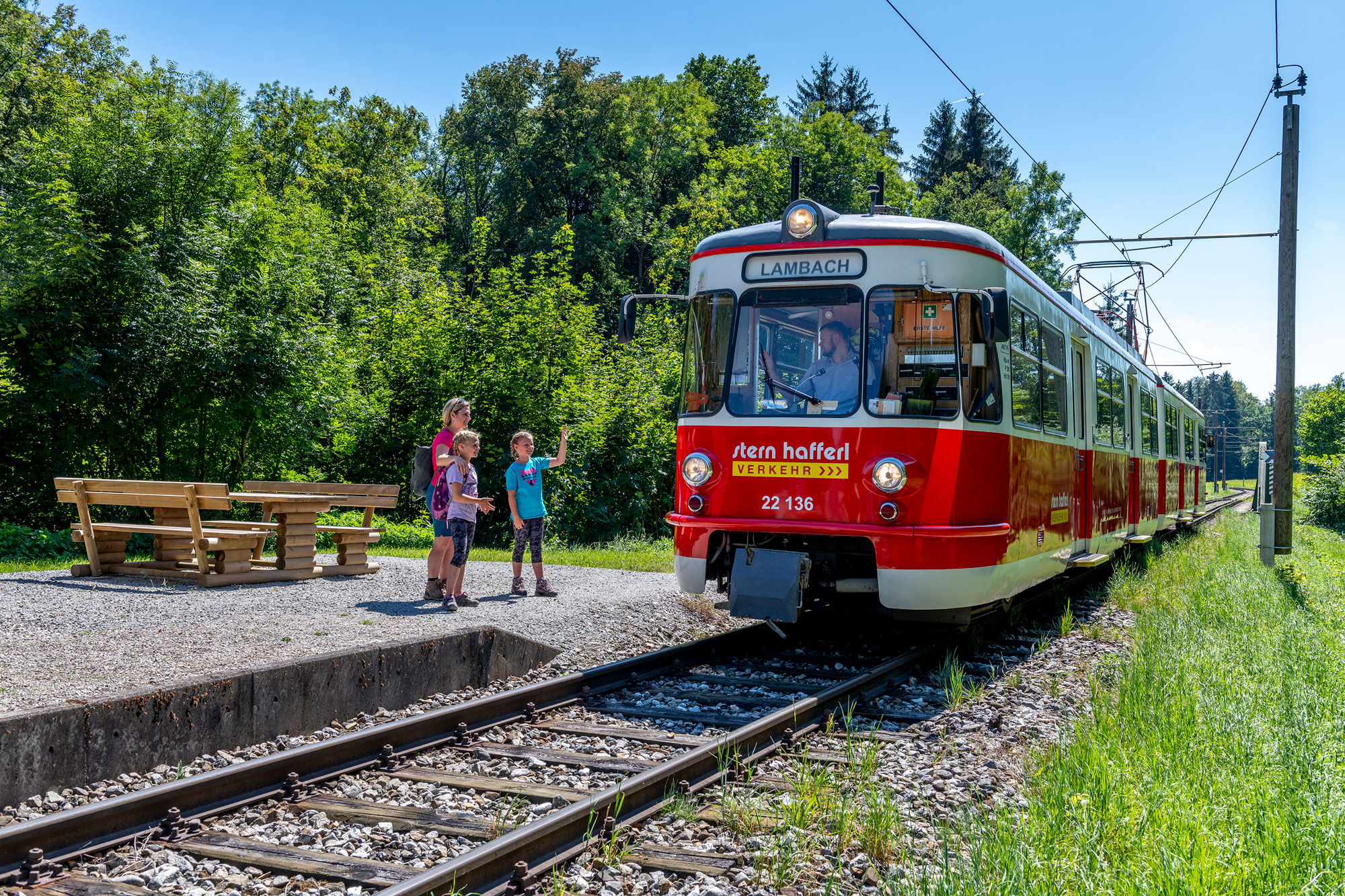 die Vorchdorferbahn im Grünen, der Triebfahrzeugführer winkt 2 kleinen Mädchen und ihrer Mutter