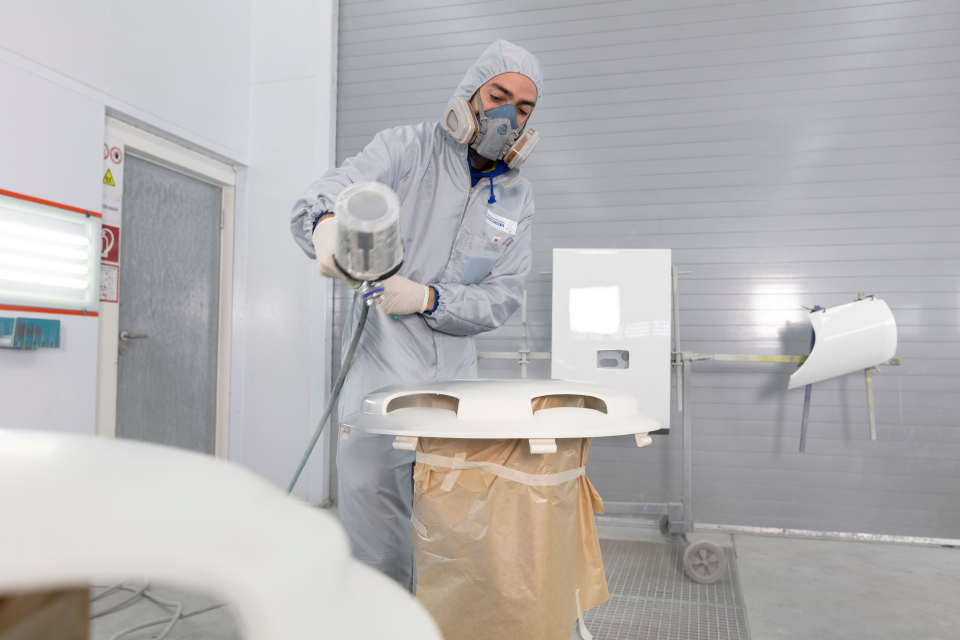 Ein Mitarbeiter lackiert ein Teil in der Lackierhalle