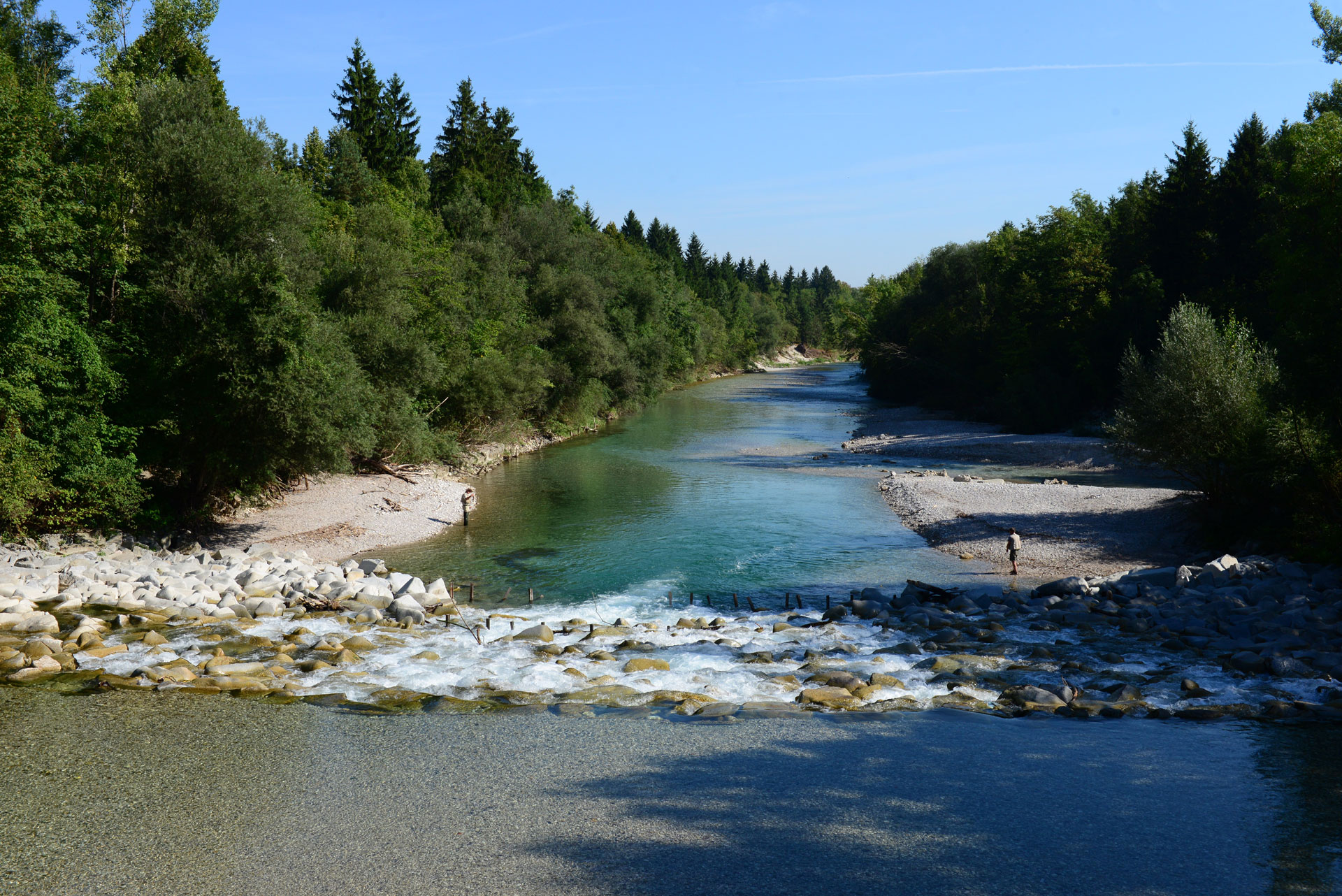 die Alm mit Steinbänken und 2 Fischern, runderum ist Wald